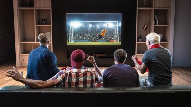 Czterech mężczyzn siedzących na kanapie i oglądających mecz piłki nożnej w telewizji